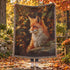 Woven cotton blanket featuring a red fox surrounded by autumn leaves in warm woodland tones