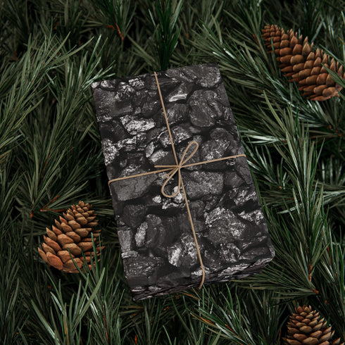 Gift wrapped in black paper with string, surrounded by pine branches and pinecones.