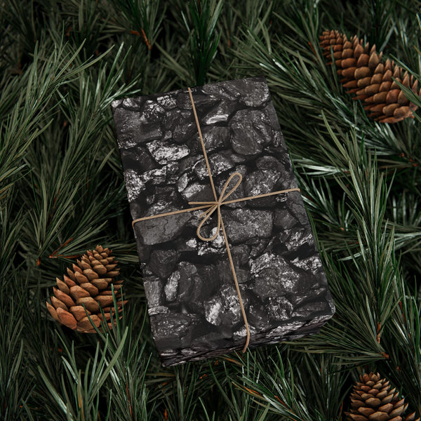 Gift wrapped in black paper with string, surrounded by pine branches and pinecones.