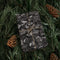 Gift wrapped in black paper with string, surrounded by pine branches and pinecones.