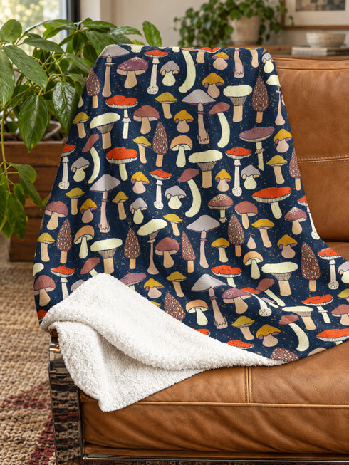 Mushroom Sherpa fleece blanket with colourful woodland toadstools on a dark navy background draped over a brown leather chair