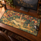 Long medieval tapestry desk mat featuring a unicorn, hunting hounds, courtly figures and a central fountain on a dark wooden study desk