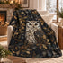 A cozy living room scene with a cream armchair draped in a soft throw blanket featuring a large owl, holly leaves, berries, and snowflakes on a dark background.