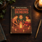 Vintage-style Summoning Demons hard backed journal featuring retro children gathered around a candlelit pentagram on a dark wooden gothic writing desk