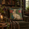 A decorative square throw pillow featuring a cream-colored rabbit on a teal and pink floral background, styled on an olive green armchair in a cozy, book-filled room.