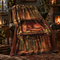 A cozy green armchair in a warmly lit living room is draped with a printed blanket featuring a sleeping red dragon resting on an open book among vintage book spines and autumn leaves.